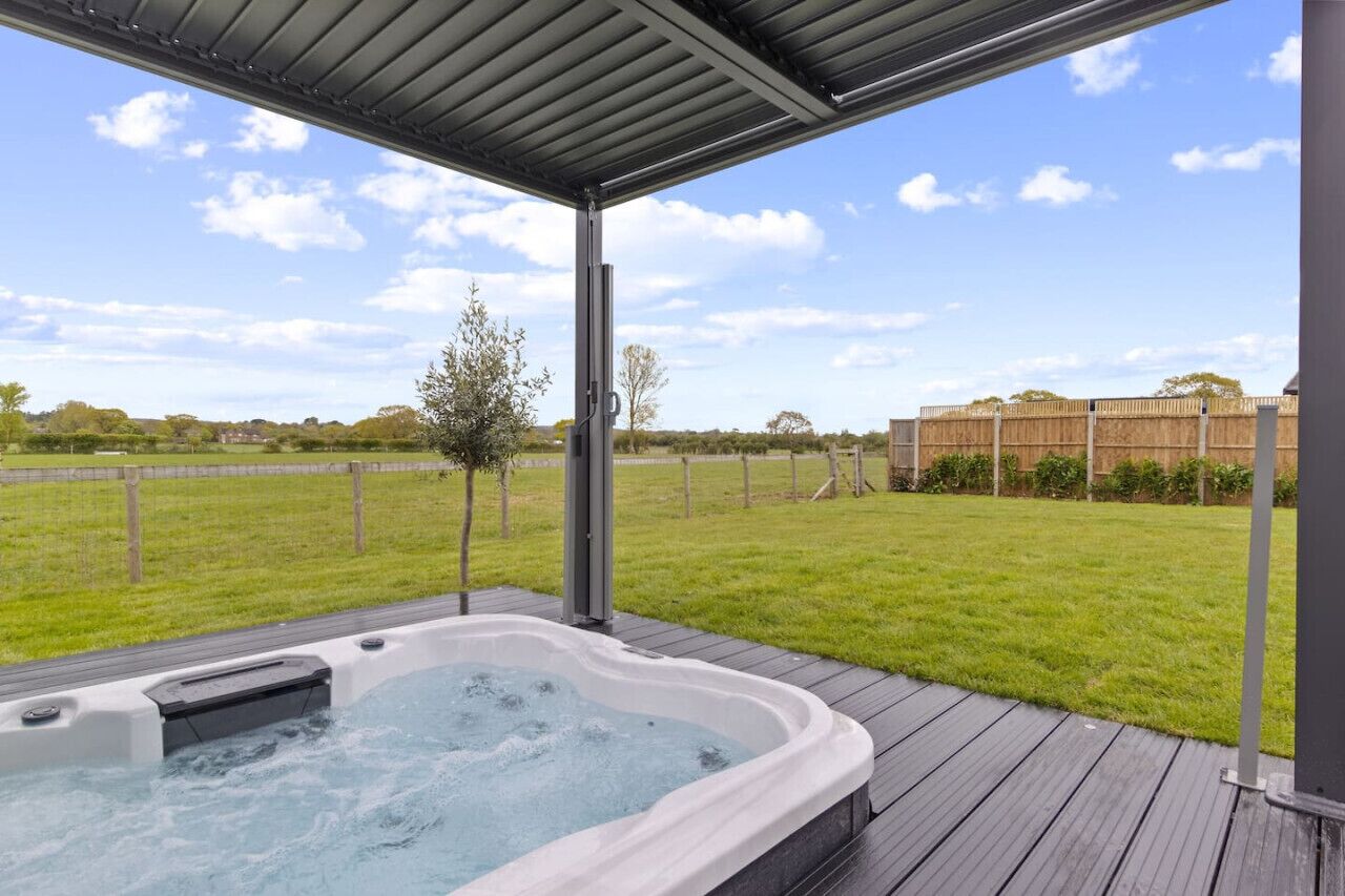 A hot tub on a wooden deck with a view of a grassy field and a wooden fence.