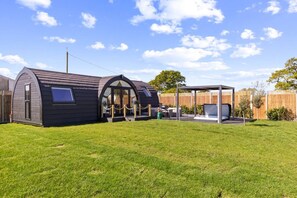 A modern, compact house with a curved roof and a covered outdoor seating area. - Nestledstays - The Barn House (Arundel)