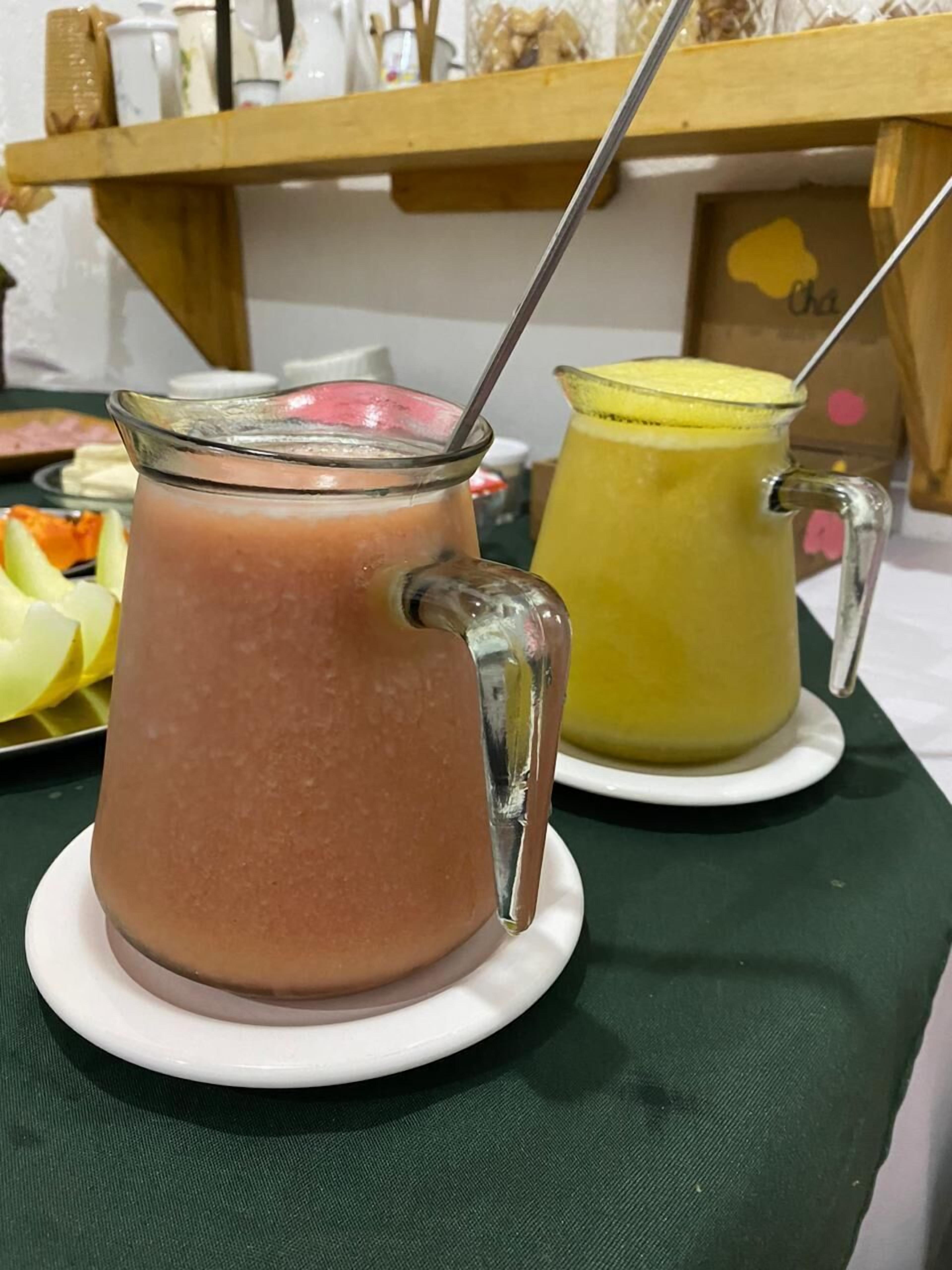 Deux carafes en verre contenant des boissons, posées sur des soucoupes blanches : l’une contient une boisson brune et l’autre, une boisson jaune. Les carafes sont sur une table recouverte d’une nappe verte.
