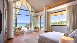 Ett modernt hotellrum med en stor säng, en soffa, ett soffbord och en TV. Rummet har stora fönster med utsikt över havet.