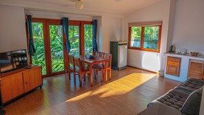 Enjoy a serene view of lush greenery from the large window in this cozy living space with a dining area and kitchenette.