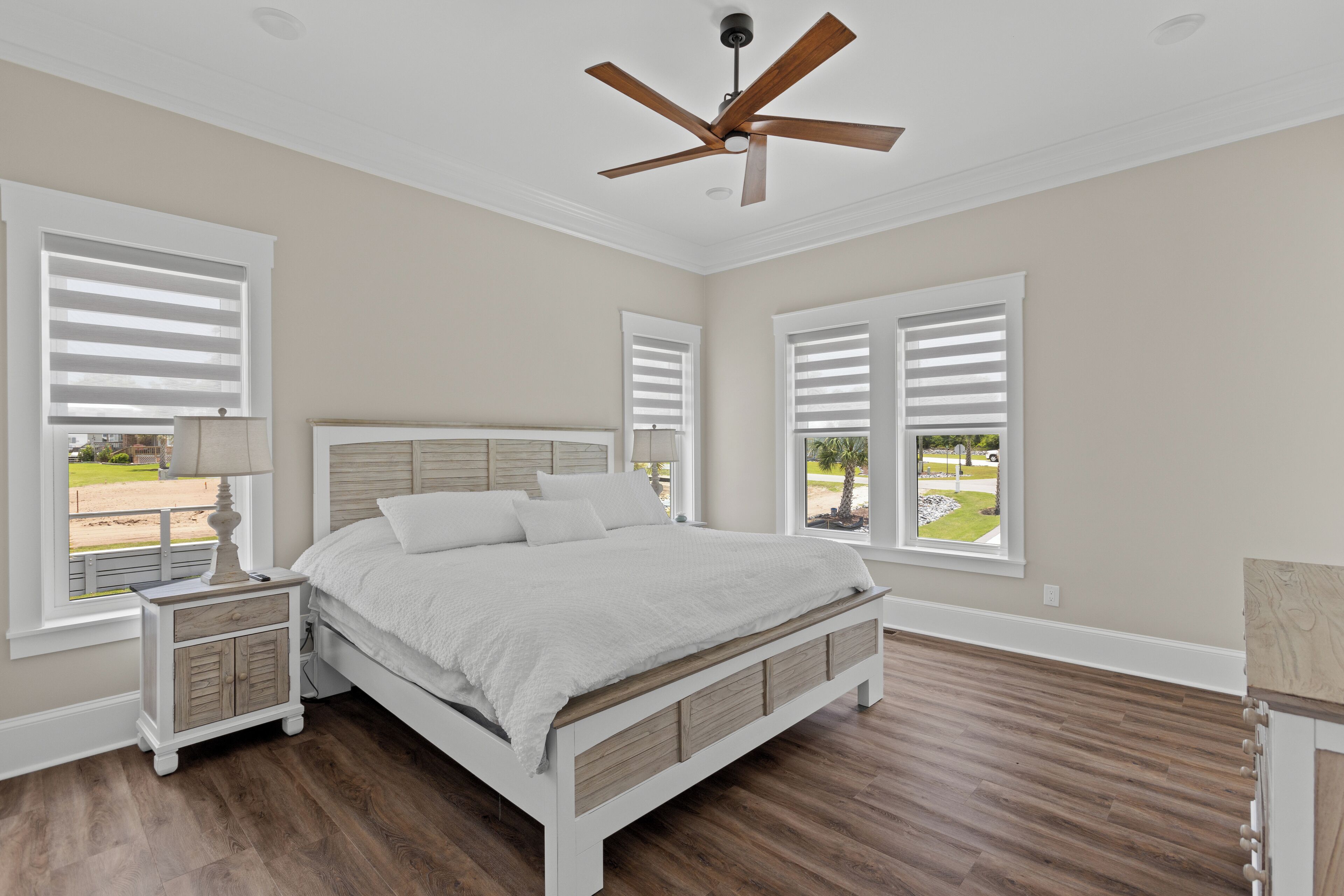 A bedroom with a bed, nightstands, a ceiling fan, and large windows.