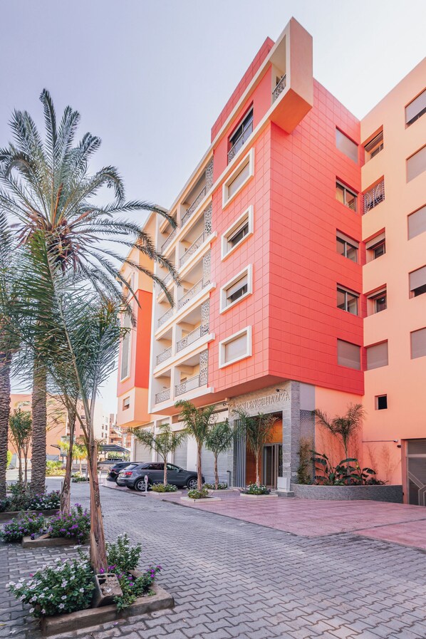 Un hotel de varios pisos con fachada roja, balcones y un patio empedrado con palmeras y plantas.