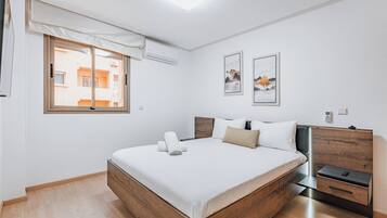 A modern bedroom with a wooden bed, a bedside table, and a window with a view of buildings.