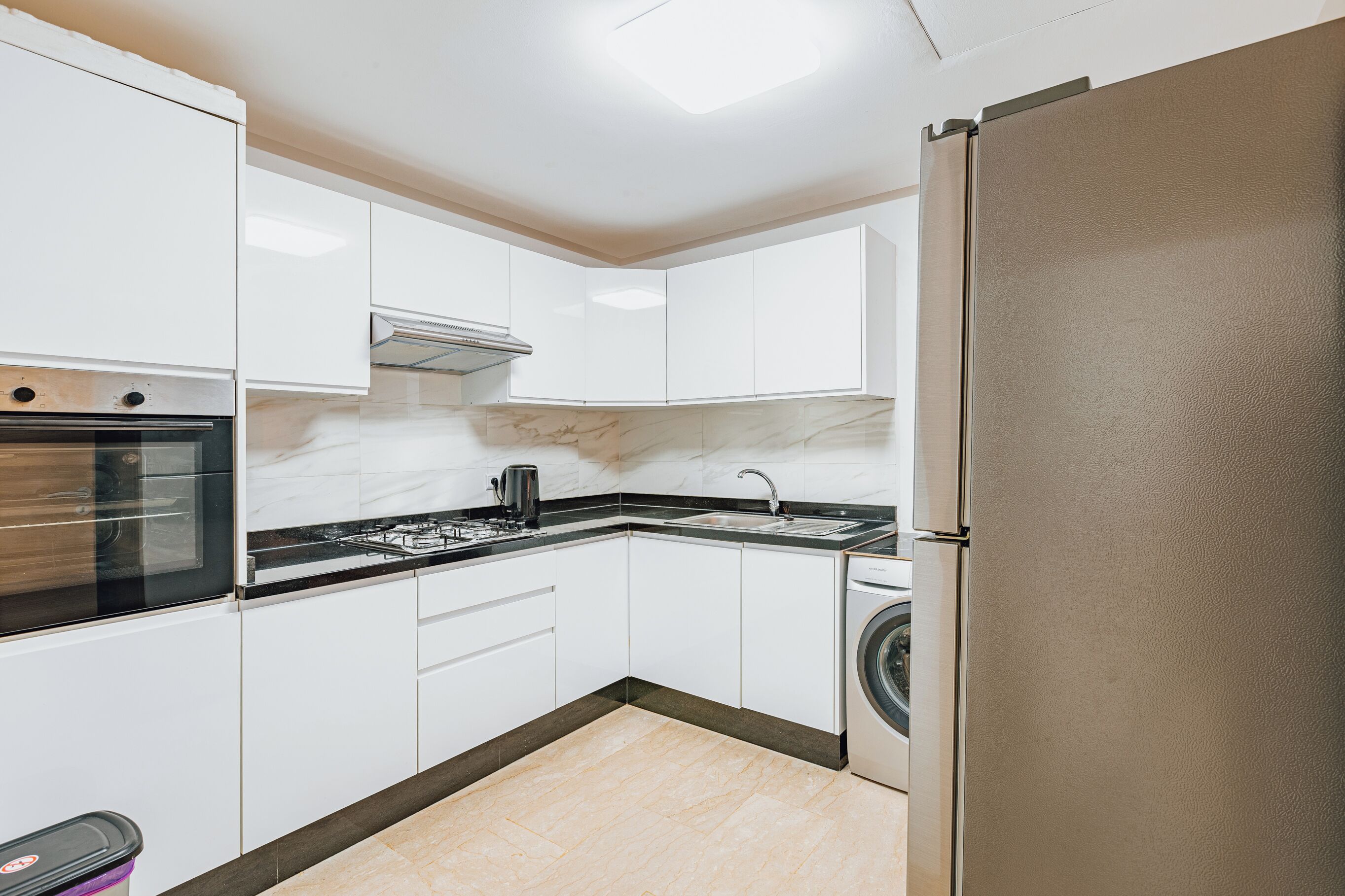 A compact kitchen with white cabinets, a stainless steel oven, a gas stove, a sink, and a washing machine.
