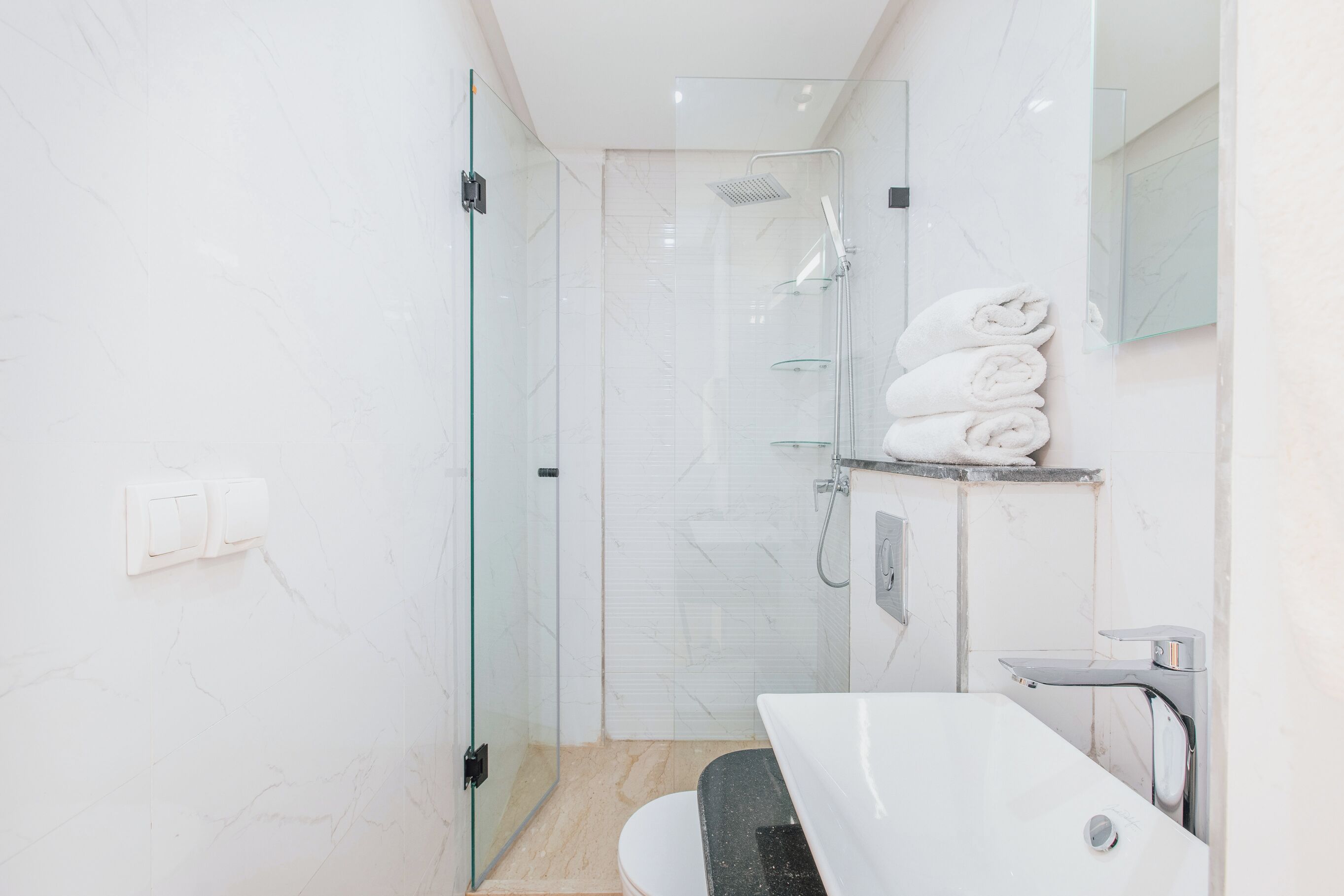 A modern bathroom with a glass-enclosed shower, a white sink, and a towel rack.