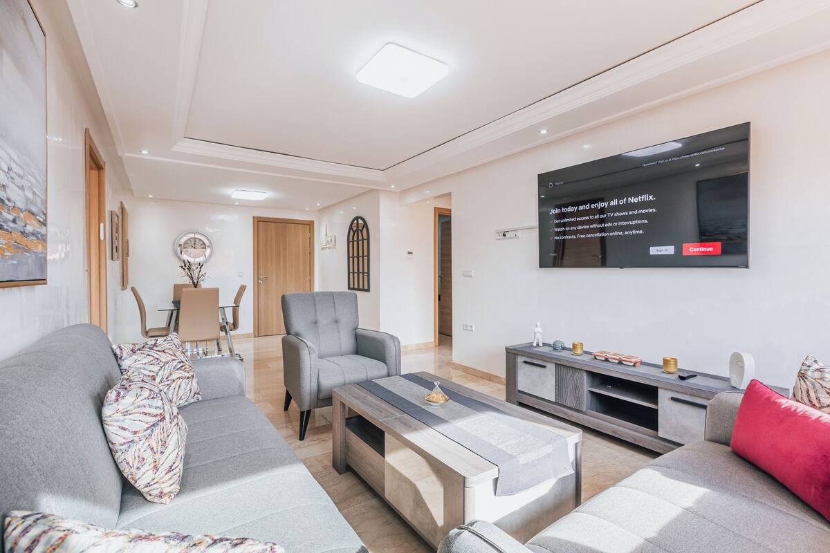 Un salon moderne avec un canapé gris, une table basse et un téléviseur fixé au mur.