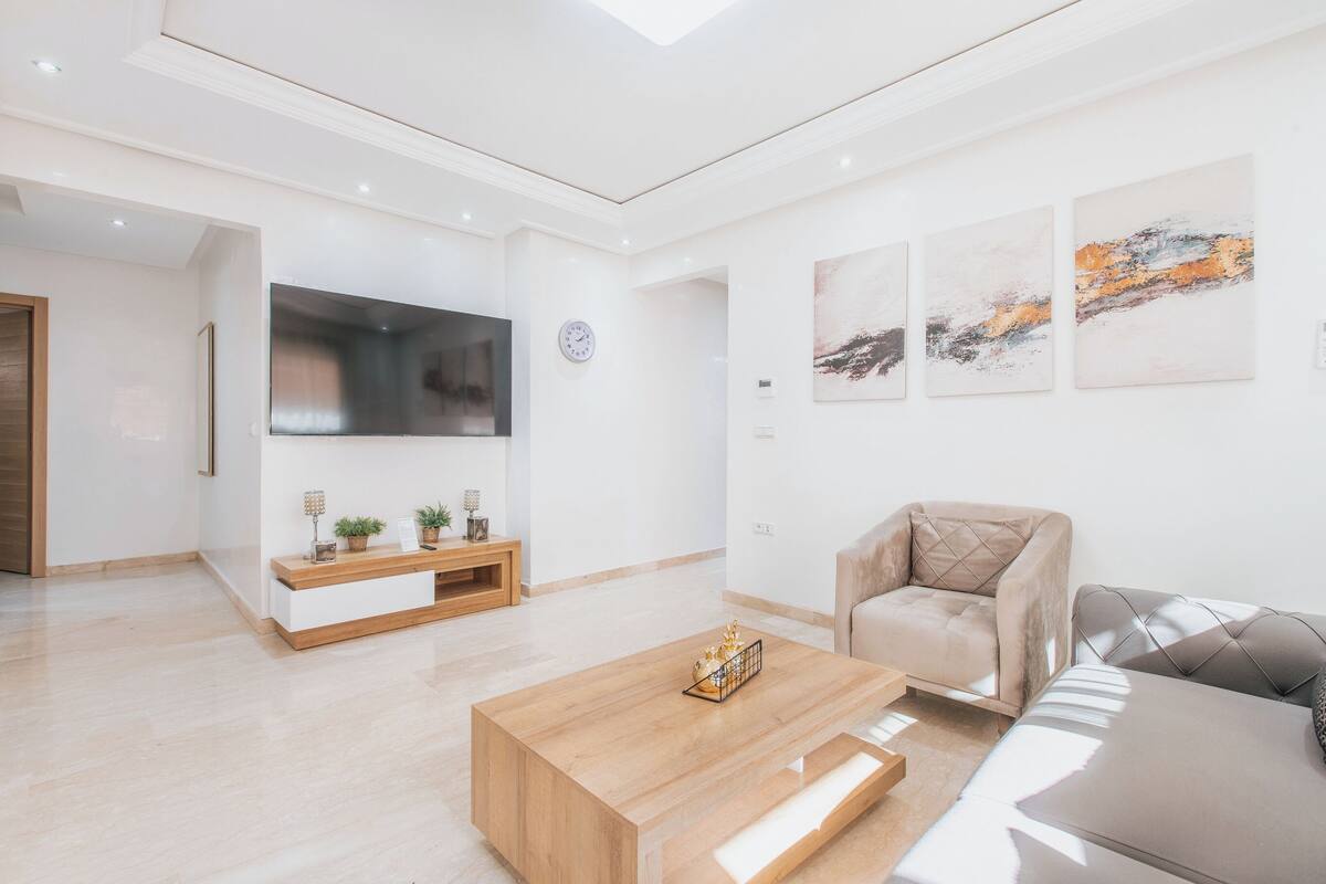 Un salon moderne avec une table basse en bois, un canapé beige et un téléviseur à écran plat fixé au mur.