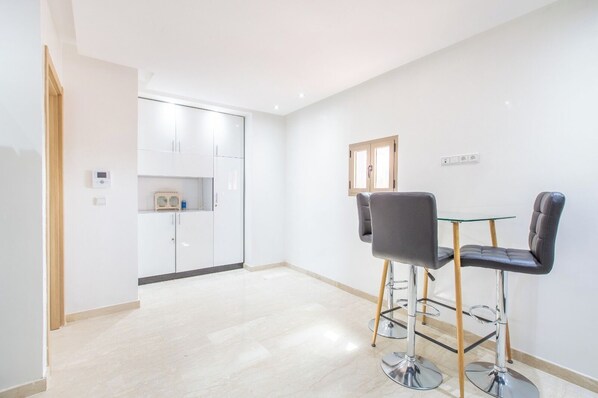 A modern, minimalistic room with a dining area featuring two chairs and a glass table, a white wardrobe, and a small kitchenette. - Migdal Gueliz Apart Hôtel, by résidence Hamza (Marrakech)