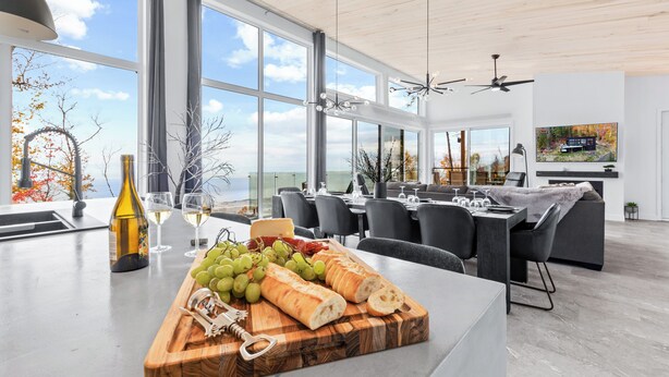 Une cuisine moderne dotée d’un grand îlot central, d’un coin repas avec des chaises noires et d’une vue sur l’océan.