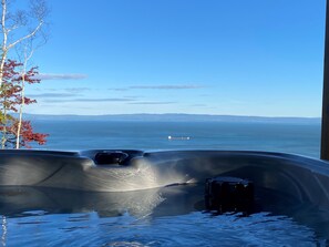 A hot tub with a view of the ocean and distant land. - New chalet with contemporary look and river view! (Petite-Rivière-Saint-François)