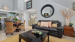 Un salon moderne avec un canapé en cuir noir, un miroir rond et un coin repas comprenant des chaises en osier et une table en bois.