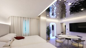 A modern hotel room with a large bed, a dining area with a table and chairs, a flat-screen TV mounted on the wall, and a ceiling with a unique reflective design. - Seoul Inn Hotel by the Designers (Seoul)
