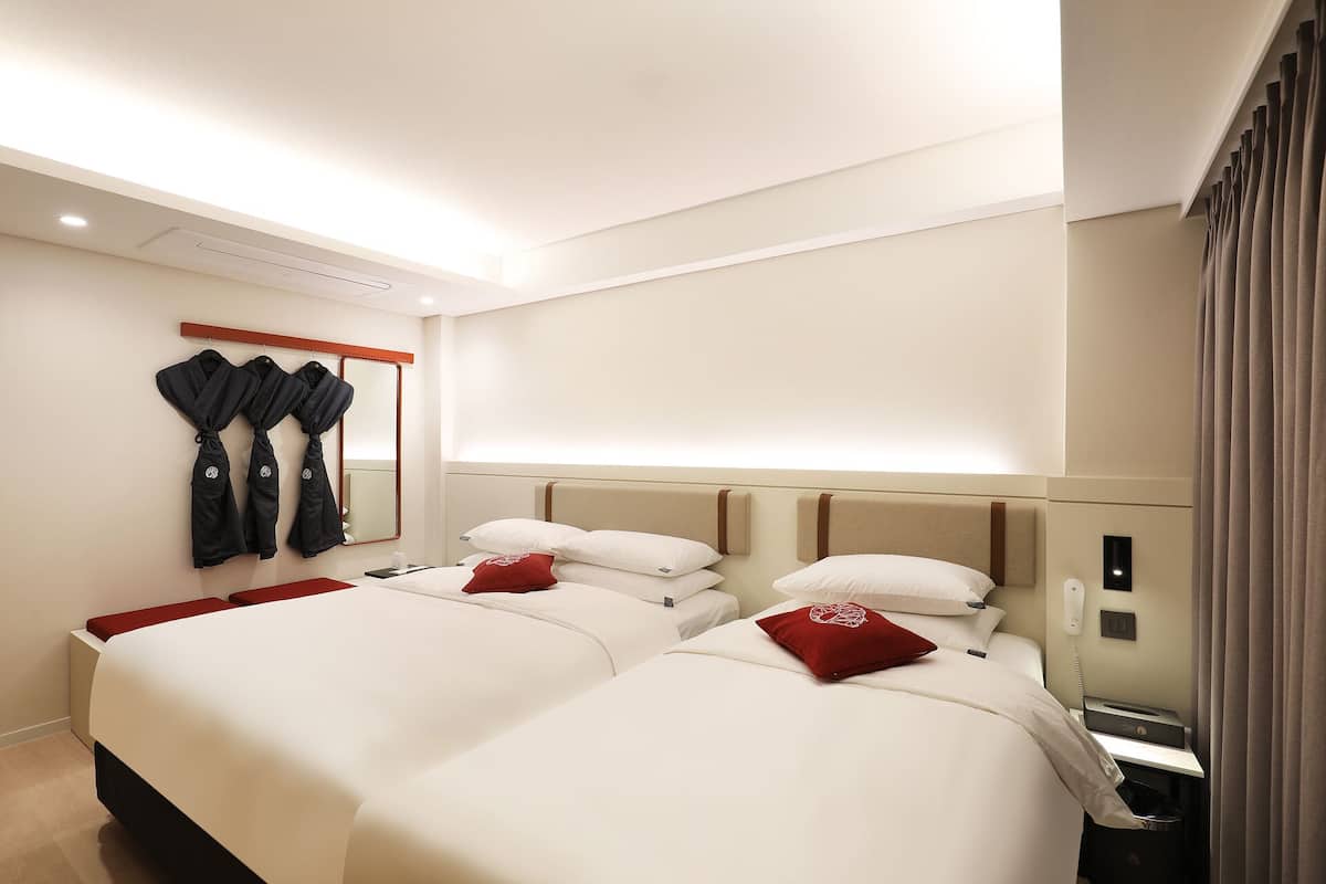 Ein Hotelzimmer mit zwei Betten, einem Spiegel, einem Kleiderständer und einem Telefon.