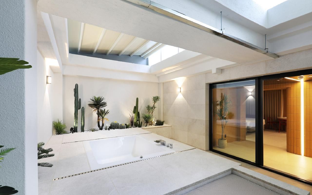 A modern interior with a large bathtub, a skylight, and a glass door leading to a room.