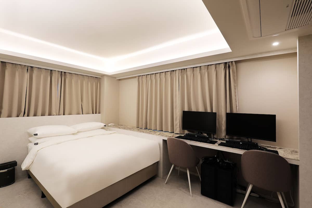 Ein modernes Hotelzimmer mit einem großen Bett, einem Schreibtisch mit zwei Stühlen, einem Flachbildfernseher und einer Deckenleuchte.
