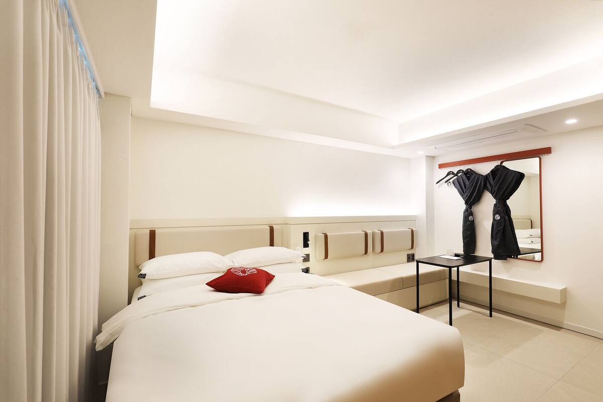 Ein Hotelzimmer mit einem großen Bett, einem Nachttisch, einem Spiegel und einem an der Wand hängenden Bademantel.