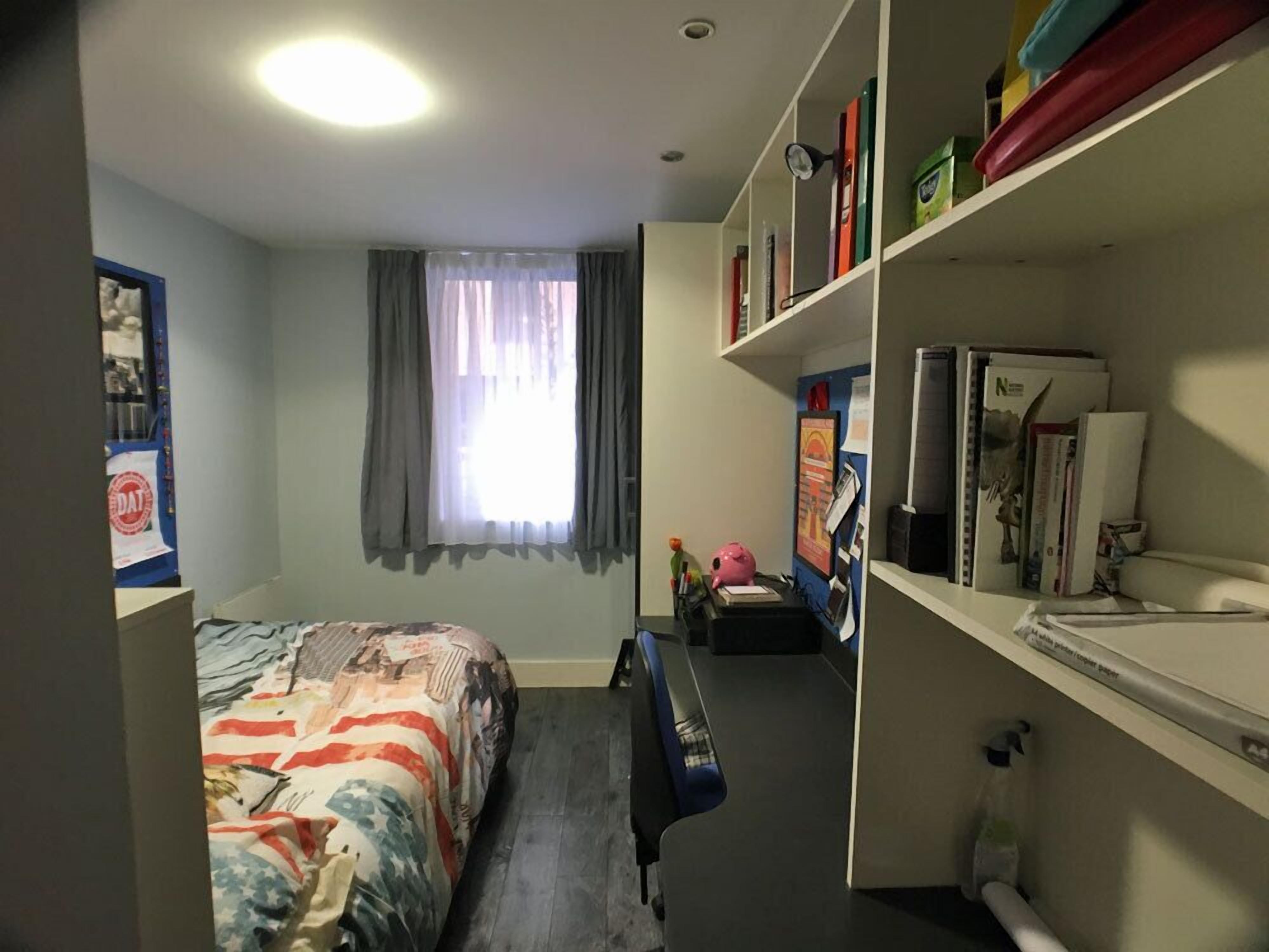 Een hotelkamer met een bed, een bureau, een boekenplank en een raam met gordijnen.