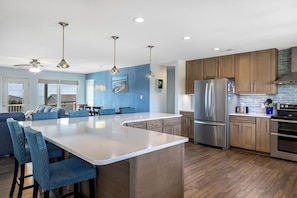 Una cocina moderna con una isla central, armarios de madera y electrodomésticos de acero inoxidable, además de sillas tapizadas en azul.
