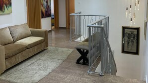 A modern living room with a beige sofa, a staircase, and a chandelier. - Signature apartments  (Lekki)
