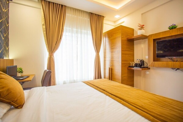 A hotel room with a bed, a desk with a laptop, a chair, a TV mounted on the wall, and a window with curtains. - ELLEGANT INN (Bengaluru)