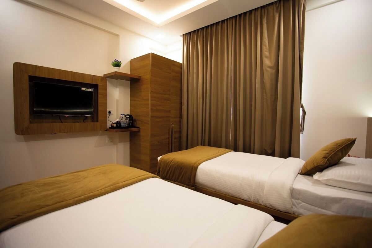 Ein Hotelzimmer mit zwei Betten, einem an der Wand befestigten Fernseher, einem Holzschrank und einem großen Fenster mit Vorhängen.
