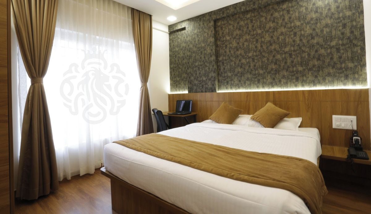 A hotel room with a large bed, a desk with a laptop, a nightstand, and a wall-mounted TV.