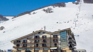 A multi-story hotel with balconies, a ski lift in the background, and a snowy mountain slope. - Hotel Pizzalto (Roccaraso)