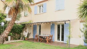 A patio with a table and chairs, surrounded by a garden and a building with blue shutters. - The vacation home, close to town, sea and mountains (Montpellier)