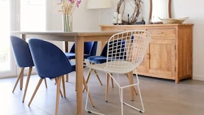 A dining area with a wooden table, two blue chairs, a white wire chair, and a wooden cabinet with a mirror and decorative items. - The vacation home, close to town, sea and mountains (Montpellier)