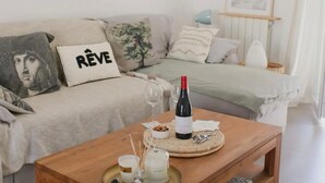 A cozy living room with a wooden coffee table, a sofa with decorative pillows, a wine bottle, and a glass. - The vacation home, close to town, sea and mountains (Montpellier)
