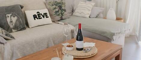A cozy living room with a wooden coffee table, a sofa with decorative pillows, a wine bottle, and a glass.