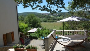 Eine Hängematte auf einer Steinterrasse mit Blick auf eine grüne Landschaft und ein kleines Dorf in der Ferne.