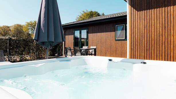 Un bain à remous avec une terrasse en bois, une table avec des chaises et un grand parasol.