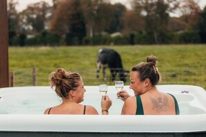 Two individuals in a hot tub with a grassy field and a cow in the background.