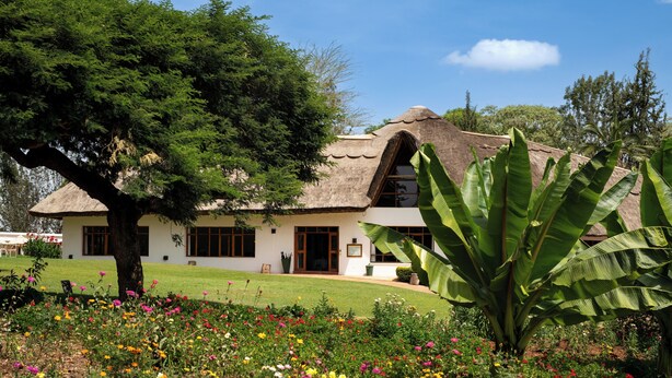 A thatched-roof house with a garden in front. - Ngorongoro Farm House (Karatu)