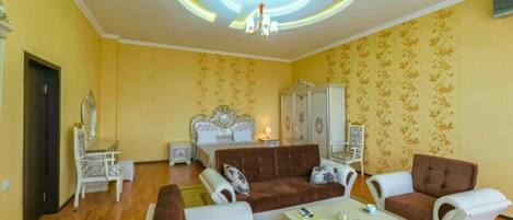 A room with a bed, two sofas, a white coffee table, and a chandelier.