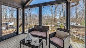 A sunroom with large windows, wicker furniture, and a view of a wooded area.