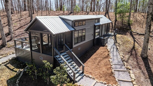 A modern cabin with a large deck, a covered porch, and a staircase leading to the main entrance.