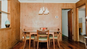 A dining area with a wooden table and chairs, a hanging light fixture, and a wooden wall. - Cozy Mid-Century Mod by Lake MI&Dunes with Hot Tub (Sawyer)