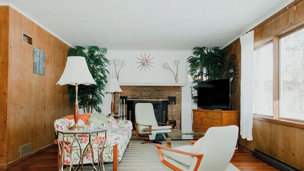 A living room with a fireplace, wooden walls, a television, and a sofa. - Cozy Mid-Century Mod by Lake MI&Dunes with Hot Tub (Sawyer)