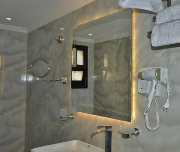 A modern bathroom with a marble wall, a large mirror, a handheld showerhead, a hairdryer, and a towel rack. - Maria Pyramids House - Superior Double or Twin Room (Giza Governorate)
