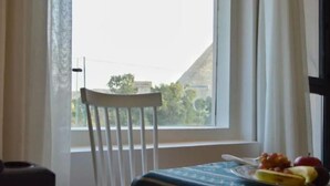 Una habitació amb una finestra, una cadira blanca i una taula amb estovall blau.