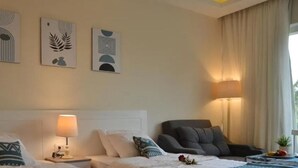 Habitació d'hotel amb un llit, una cadira i un escriptori amb una làmpada. Hi ha tres quadres a la paret sobre el llit.