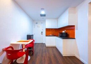 A compact kitchen with white cabinets, a black countertop, and a red chair. - Master House Centrestage PJ (Petaling Jaya)