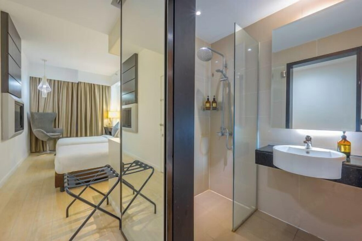 Un baño de hotel moderno con cabina de ducha de vidrio, un lavabo blanco y un espejo grande.