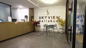 Un espace d’accueil comprenant un comptoir de réception, des chaises et un mur sur lequel est inscrit le nom « SKYVIEW Setiabud ».