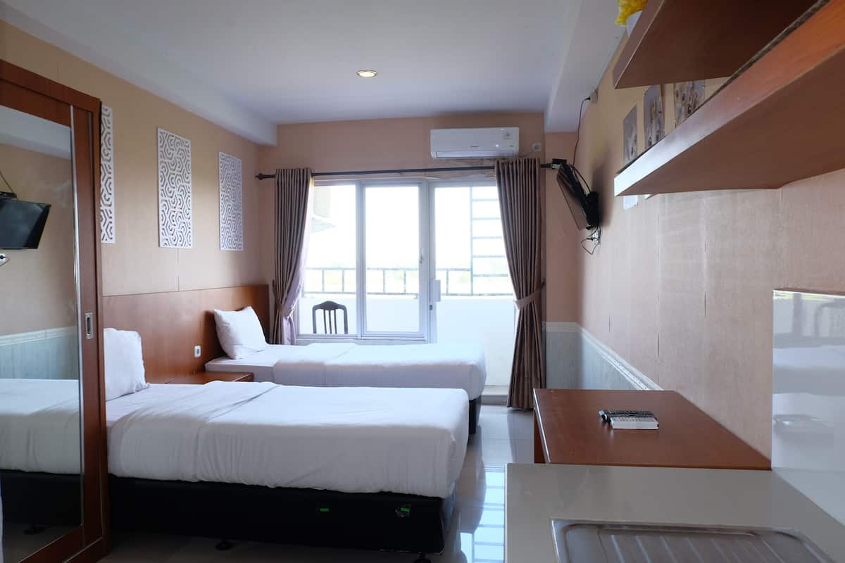 A hotel room with two beds, a desk, a chair, and a window with curtains.