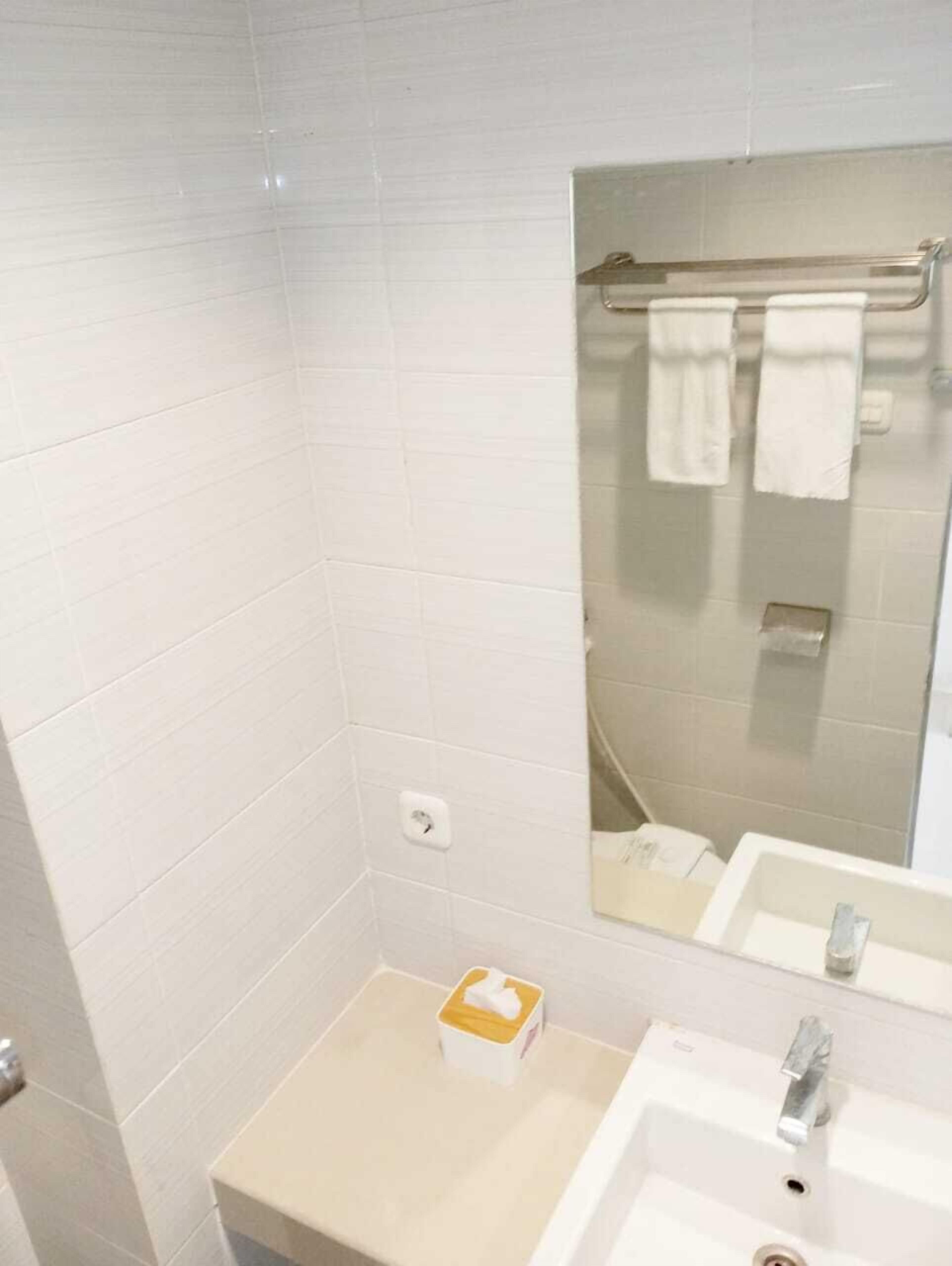 A bathroom with white tiles, a mirror, a sink, and a towel rack.