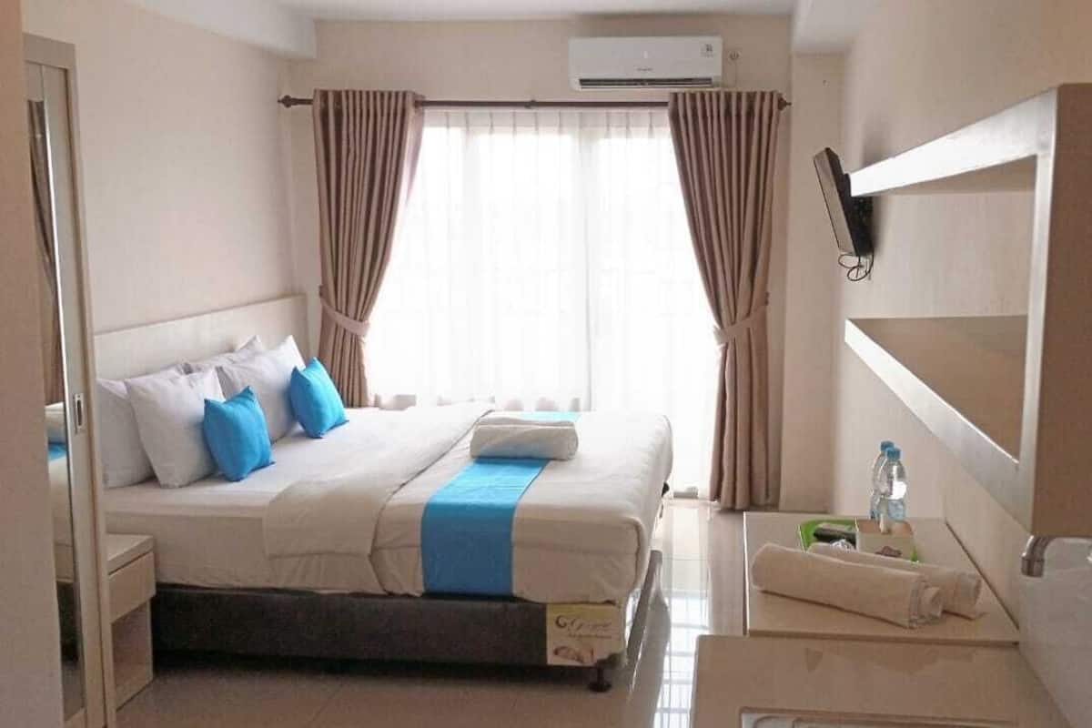 A hotel room with a bed, a desk, a chair, a mirror, and a window with curtains.
